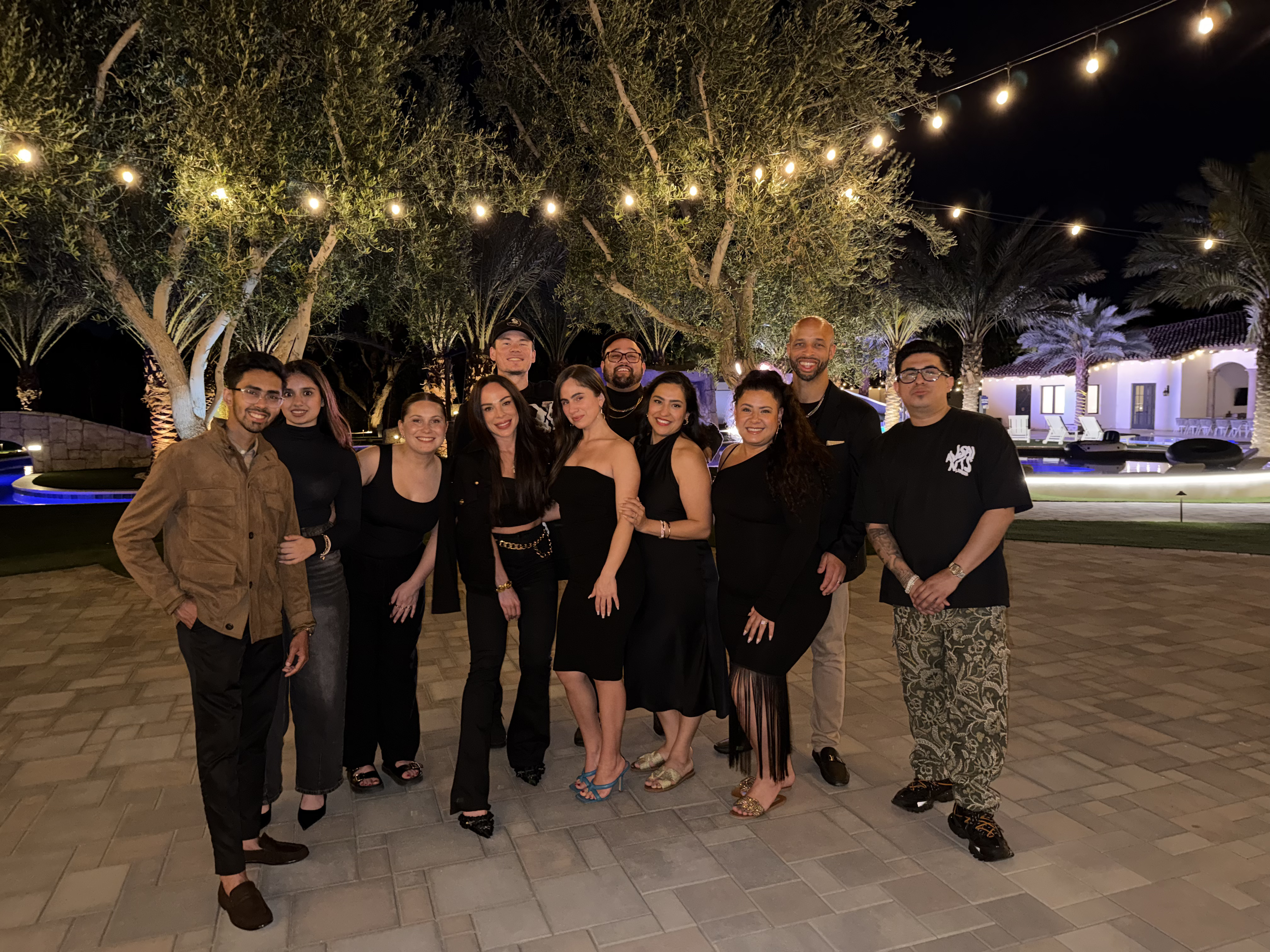 Large True Vision team gathering at an outdoor evening event with string lights, celebrating together